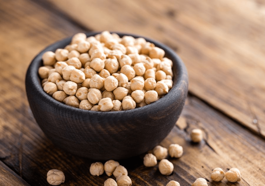 Dried chickpeas in a black bowl on a wooden surface with scattered chickpeas nearby